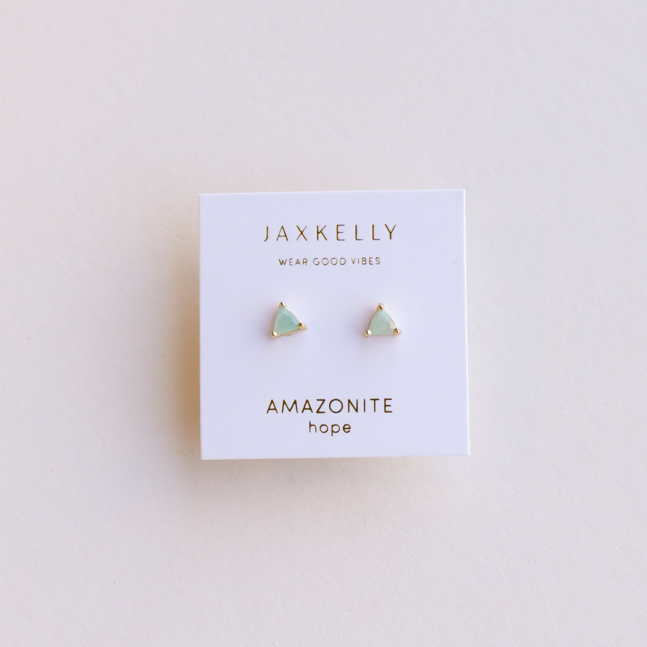 The Amazonite Mini Energy Gems - Hope are small, triangular studs with 18k gold plating and sterling silver posts, displayed on a white JaxKelly card reading WEAR GOOD VIBES, AMAZONITE, and hope against a light background.