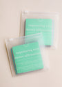 Two clear pouches each hold a stack of aqua-colored, waterproof Teens Shower Affirmations™ cards with white text, designed to inspire confidence and positivity in teens every time they shower.