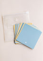 A translucent zippered pouch sits on a light surface next to a fanned-out stack of Note To Self Shower Affirmations™ cards in pastel blue and yellow, each featuring a small white plant icon in the corner.