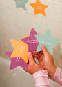 A child holds Kids Shower Affirmations™—waterproof cards with positive quotes like “I can do hard things,” “I dream big and reach for the stars,” and “I am grateful”—near a wet bathroom wall.