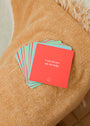 A stack of Teens Shower Affirmations™ cards for teens rests on a textured orange blanket. The top red card says, "I can always ask for help," with a small smiley face beneath the uplifting message.