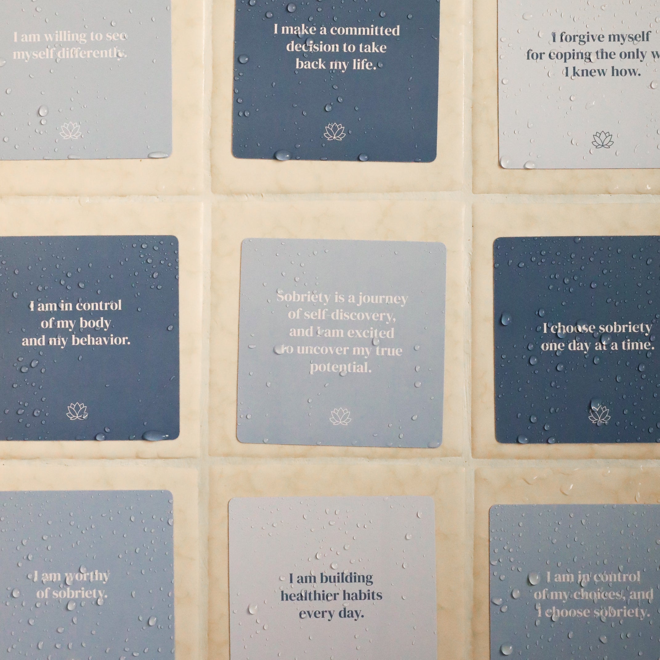 Sobriety Shower Affirmations™—nine waterproof blue and gray cards with self-control affirmations for sobriety—are arranged in a 3x3 grid on a tiled wall, each with water droplets, supporting your recovery journey.