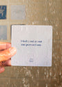 A hand holds a Sobriety Shower Affirmations™ waterproof card under running water. It reads, "I feel good about the person I am," with a lotus symbol—ideal encouragement for your recovery journey.