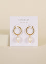 The Pearl Drop Earring features gold plated hoops with dangling freshwater pearls and sterling silver posts, displayed on a white JaxKelly card that reads “Wear Good Vibes,” set against a soft beige background.