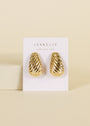 The Bold Swirl - Earring, a pair of gold plated, textured, dome-shaped statement earrings, is displayed on a white card labeled JaxKelly Wear Good Vibes against a beige background.