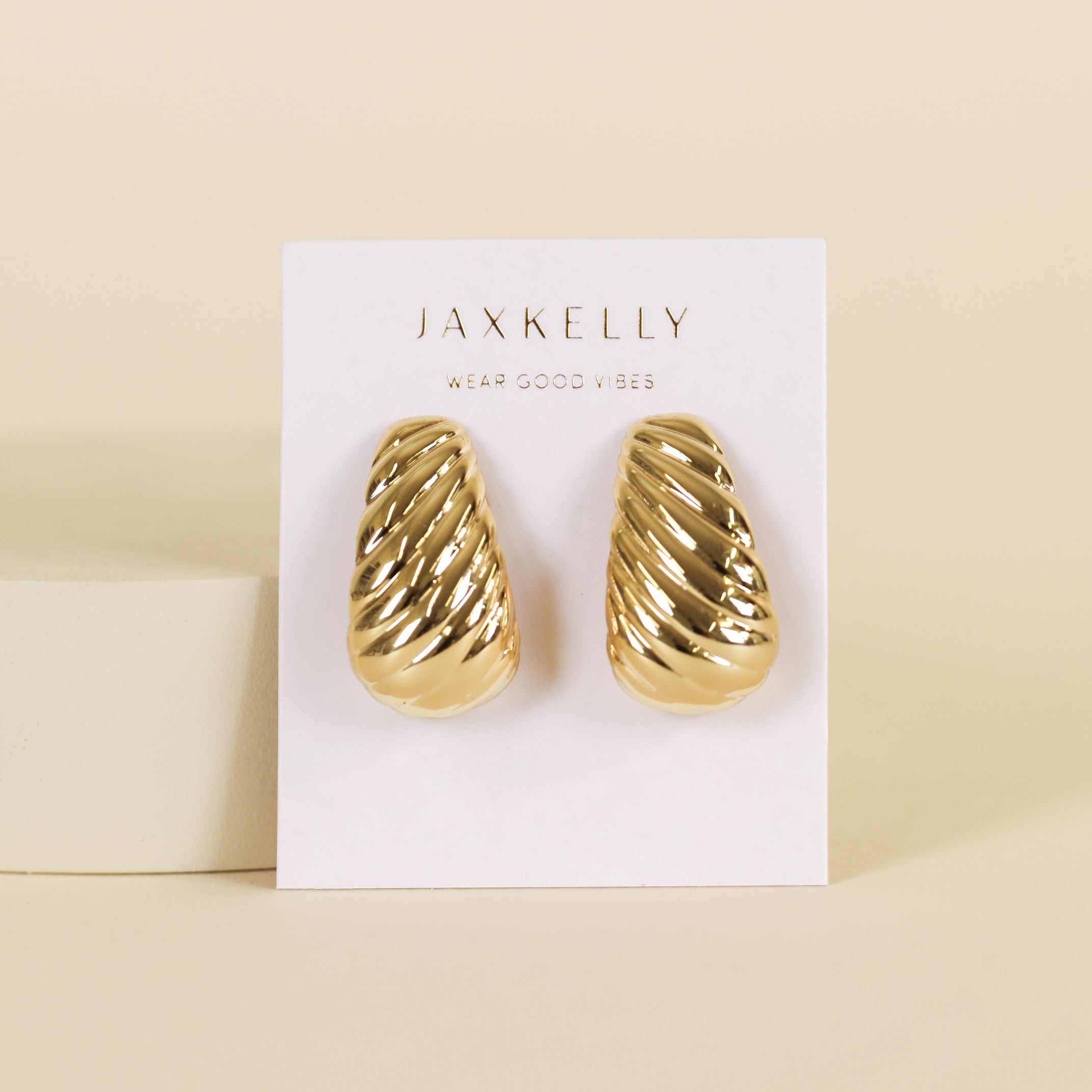 The Bold Swirl - Earring, a pair of gold plated, textured, dome-shaped statement earrings, is displayed on a white card labeled JaxKelly Wear Good Vibes against a beige background.