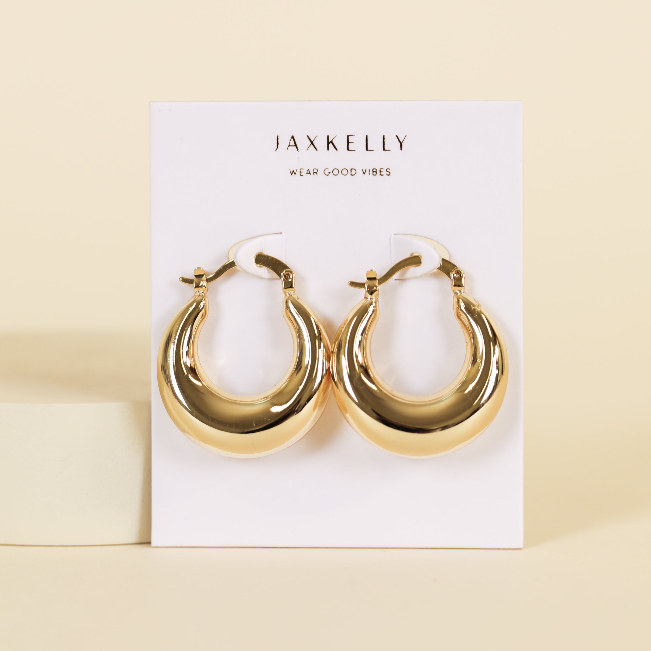 A pair of Sculptural Wide Hoop Earrings, gold plated and lightweight, displayed on a white JaxKelly Wear Good Vibes card against a beige background—perfect bold jewelry for everyday style.