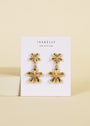Double Daisy Drop Earrings plated in gold, crafted as abstract flowers, are displayed on a white card featuring the JaxKelly brand and "Wear Good Vibes" tagline, set against a beige background.