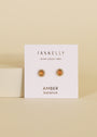Amber Sun Stud: Gold plated earrings with amber stones displayed on a white card labeled “JaxKelly Wear Good Vibes” and “Amber Balance” against a beige background.