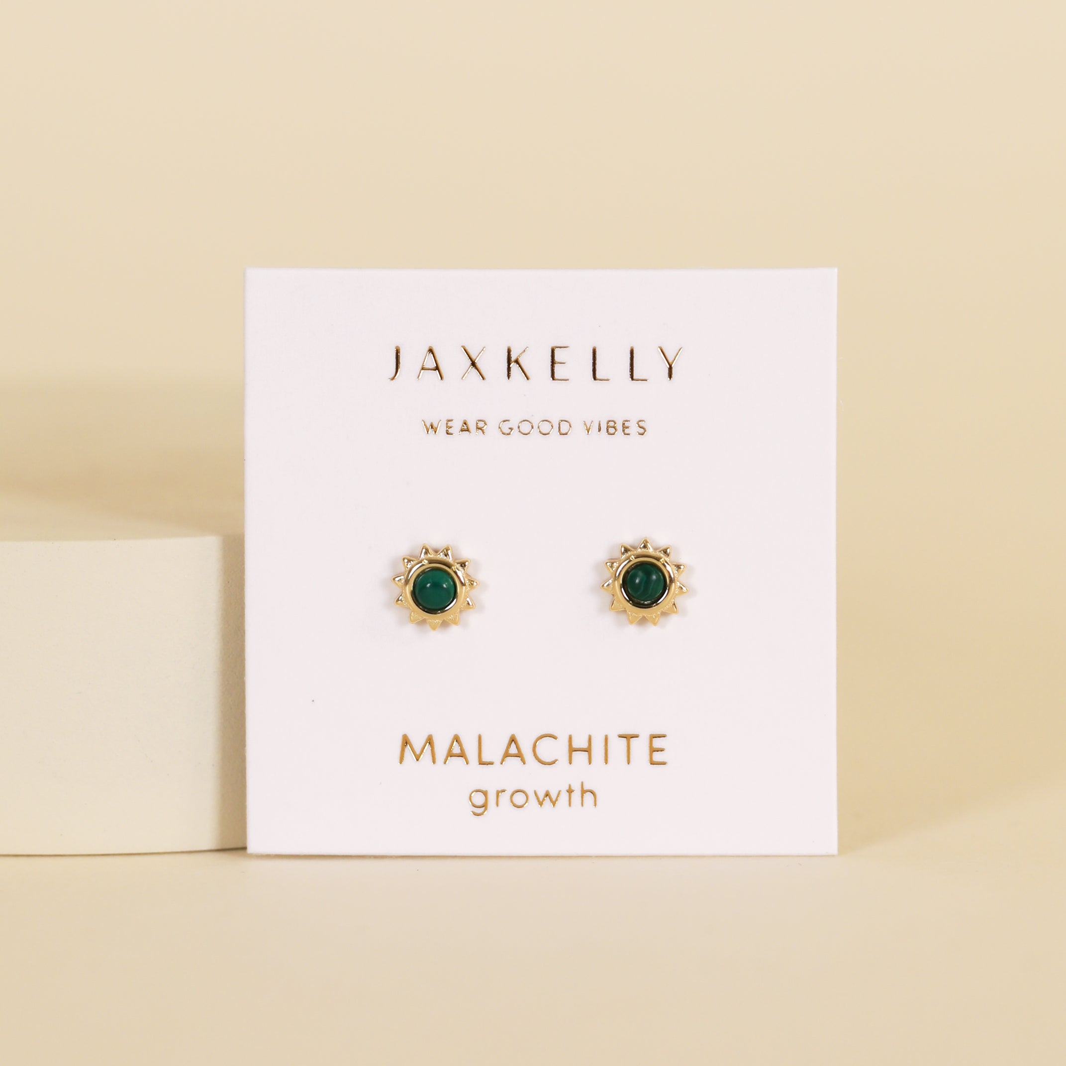 The Malachite Sun Stud features vibrant malachite stones and 18k gold plating on a white JaxKelly "Wear Good Vibes—Malachite Growth" card, displayed against a beige background.