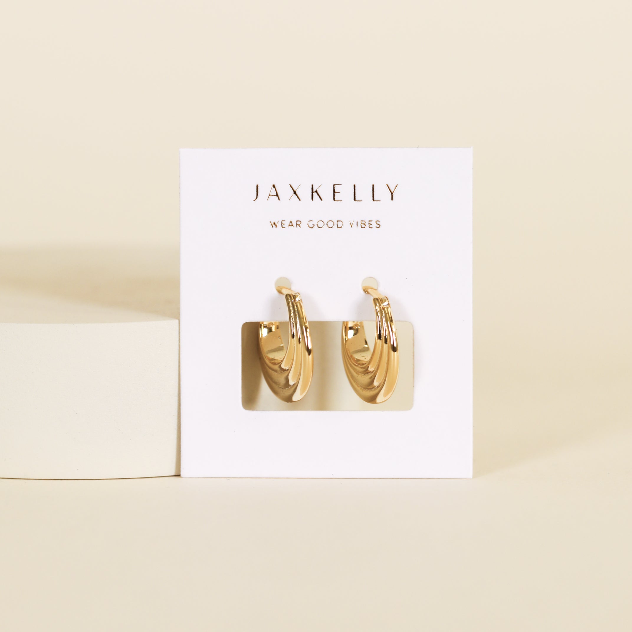 The Triple Arch Hoop - Earring features gold hoops with a twisted design, inspired by retro modern jewelry, displayed on a white JaxKelly card reading "Wear Good Vibes" against a neutral beige background.