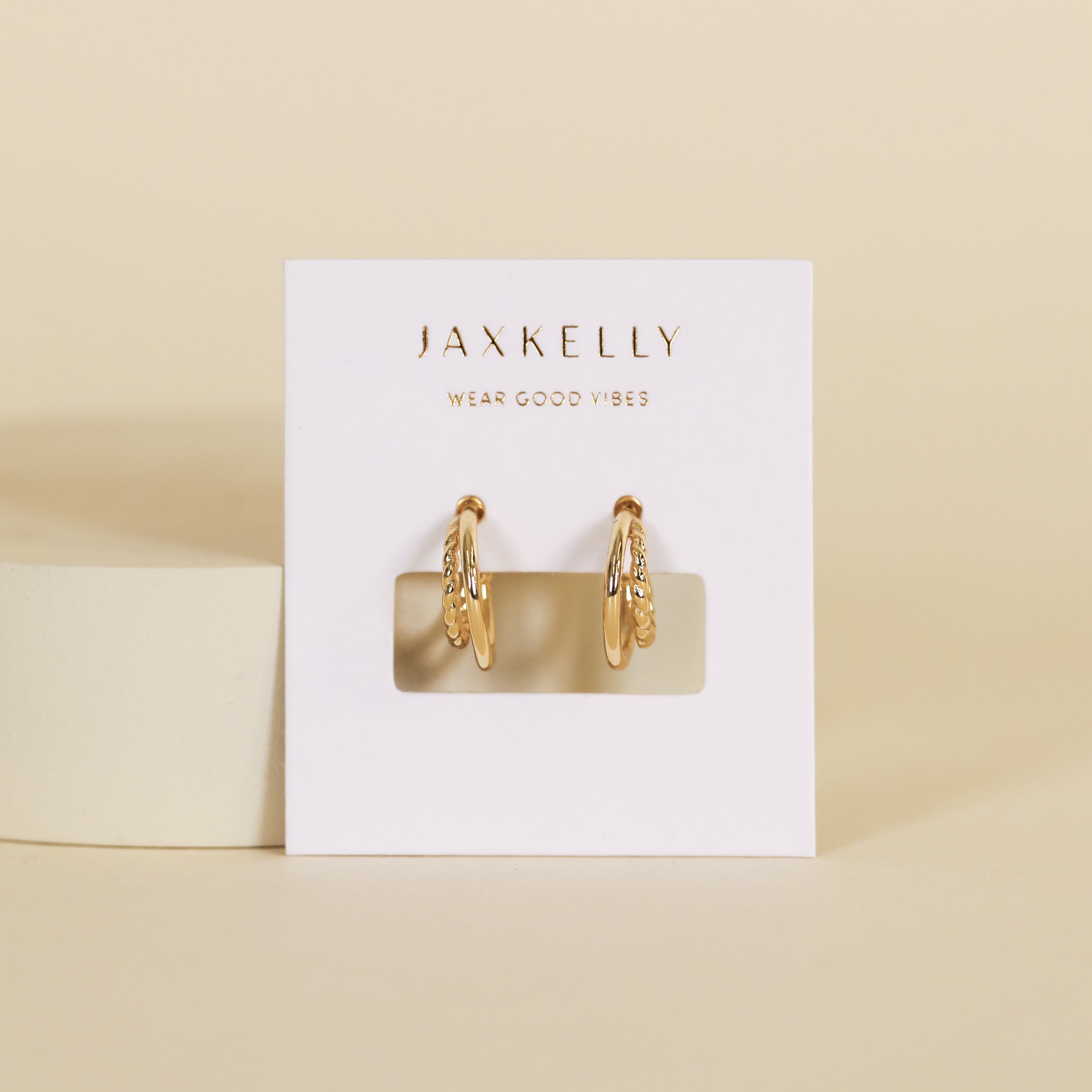 A pair of Double Hoop - Earring gold-plated with small crystal accents is displayed on a white JaxKelly Wear Good Vibes card, set against a beige background.