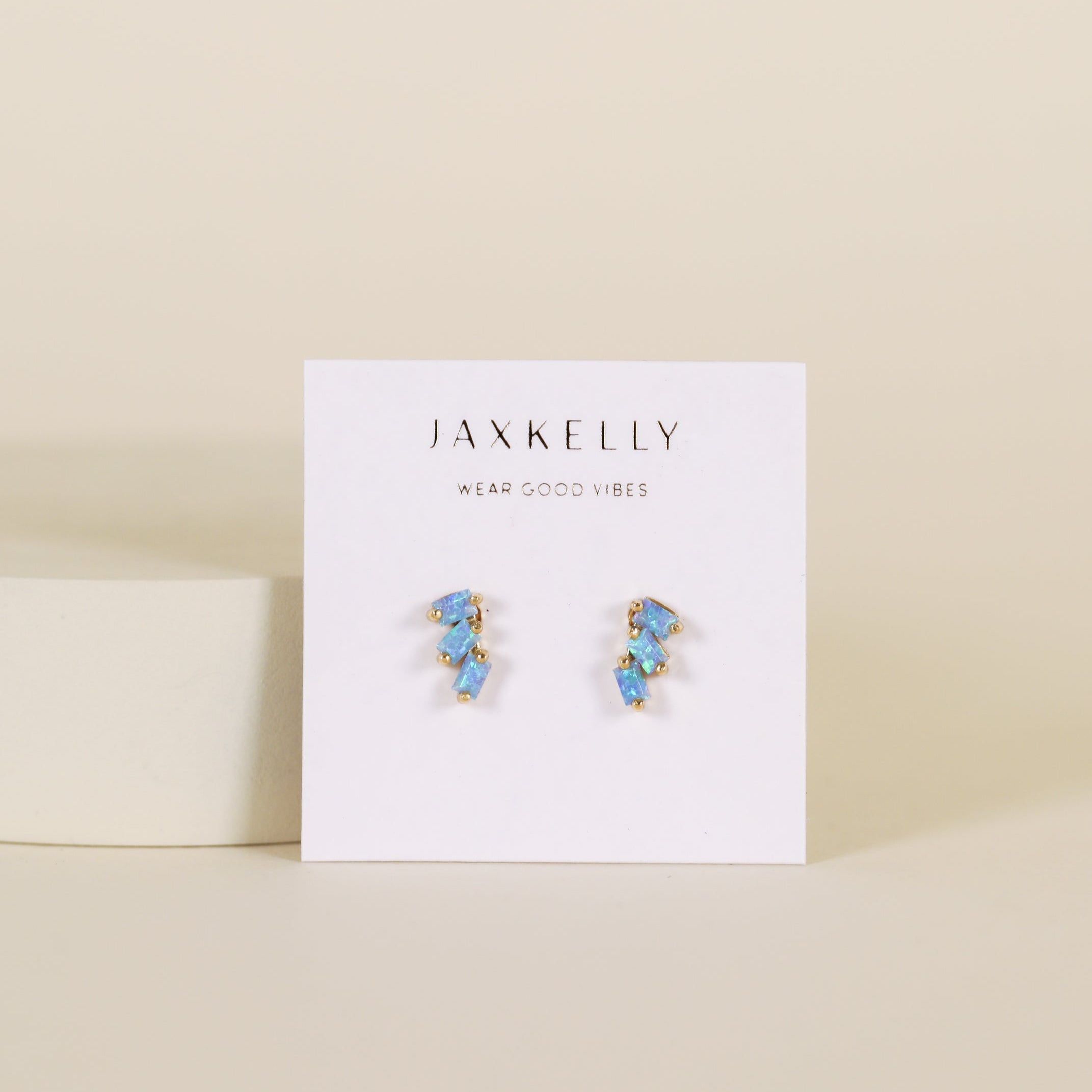 The Offset Trio - Fire Opal features gold-plated blue opal stud earrings on a white JaxKelly card with the tagline "Wear Good Vibes," displayed against a light beige background.
