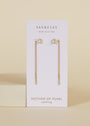 The JaxKelly Studded Threader - Mother of Pearl earrings, featuring gold chains and pearl studs with mother-of-pearl accents, are shown on a white JaxKelly card against a neutral beige background.