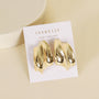 The JaxKelly Gold Bold Wave studs feature shiny, sculptural statement earrings with 18k gold plating and sterling silver posts, displayed on a white JaxKelly card with “Wear Good Vibes,” set against a light beige background.