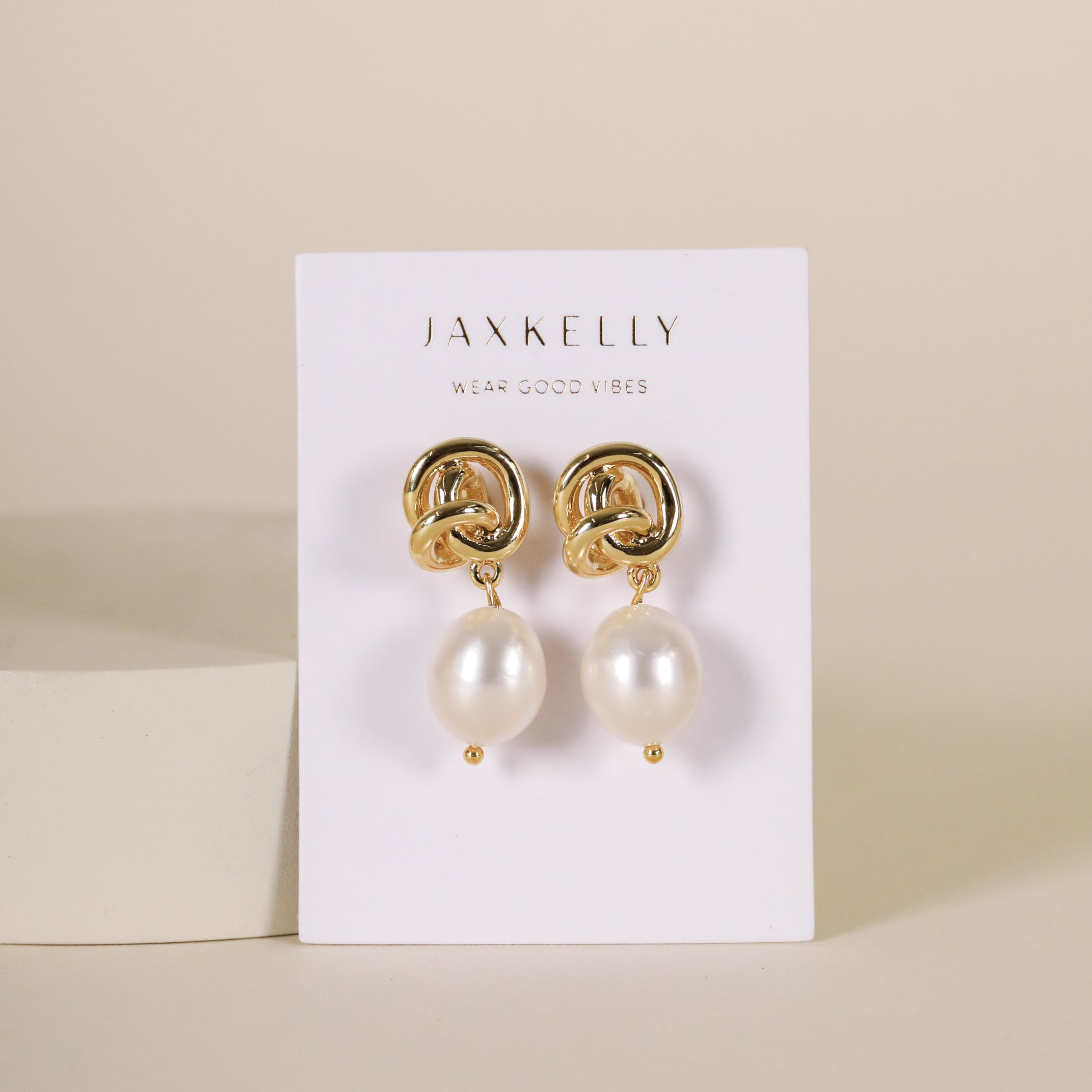The Pearl Knot - Earring features 18k gold plated knot studs with dangling freshwater pearls, displayed on a JaxKelly card against a neutral background.