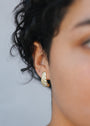 Close-up of a person with short curly dark hair wearing the Bold Swirl - Earring, a textured gold plated hoop, in their left ear, with focus on this statement jewelry against a neutral background.