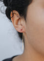 Close-up of a person’s ear with dark curly hair, wearing JaxKelly's Studded Threader - Pink CZ earring. The small pink stud and long gold threader stand out against the plain, blurred background, showcasing tarnish-free elegance.