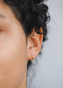 A close-up of a person's ear shows two gold hoops—one smooth, the other the sparkling Pave Spiral - Earring—with curly dark hair and part of their face softly visible in the background.