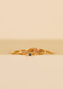 The Pinky Ring - Pink features three dainty gold bands with colorful gemstones—blue, pink cubic zirconia, and clear—stacked against a soft beige background, perfect for wearing solo on your pinky or stacking together.