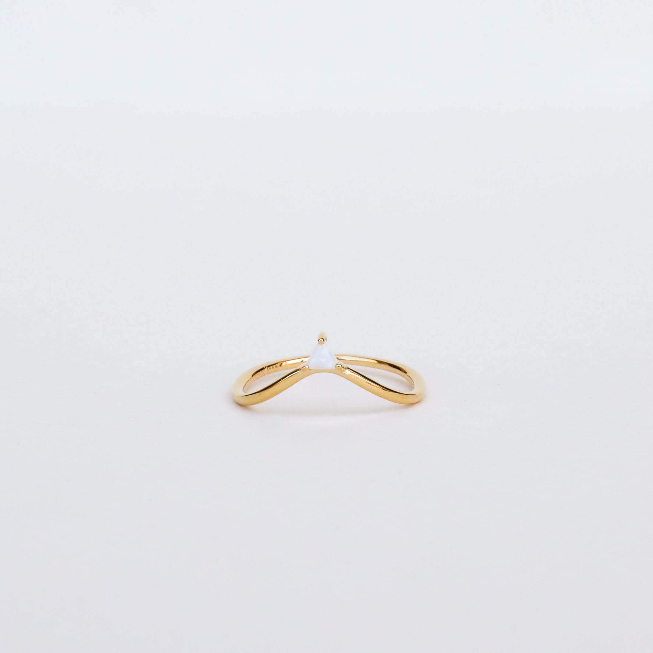 The Arched Triangle Ring - White Opal is a minimalist 18kt gold ring with a slim, open band and a small central opal, showcased elegantly against a plain white background.