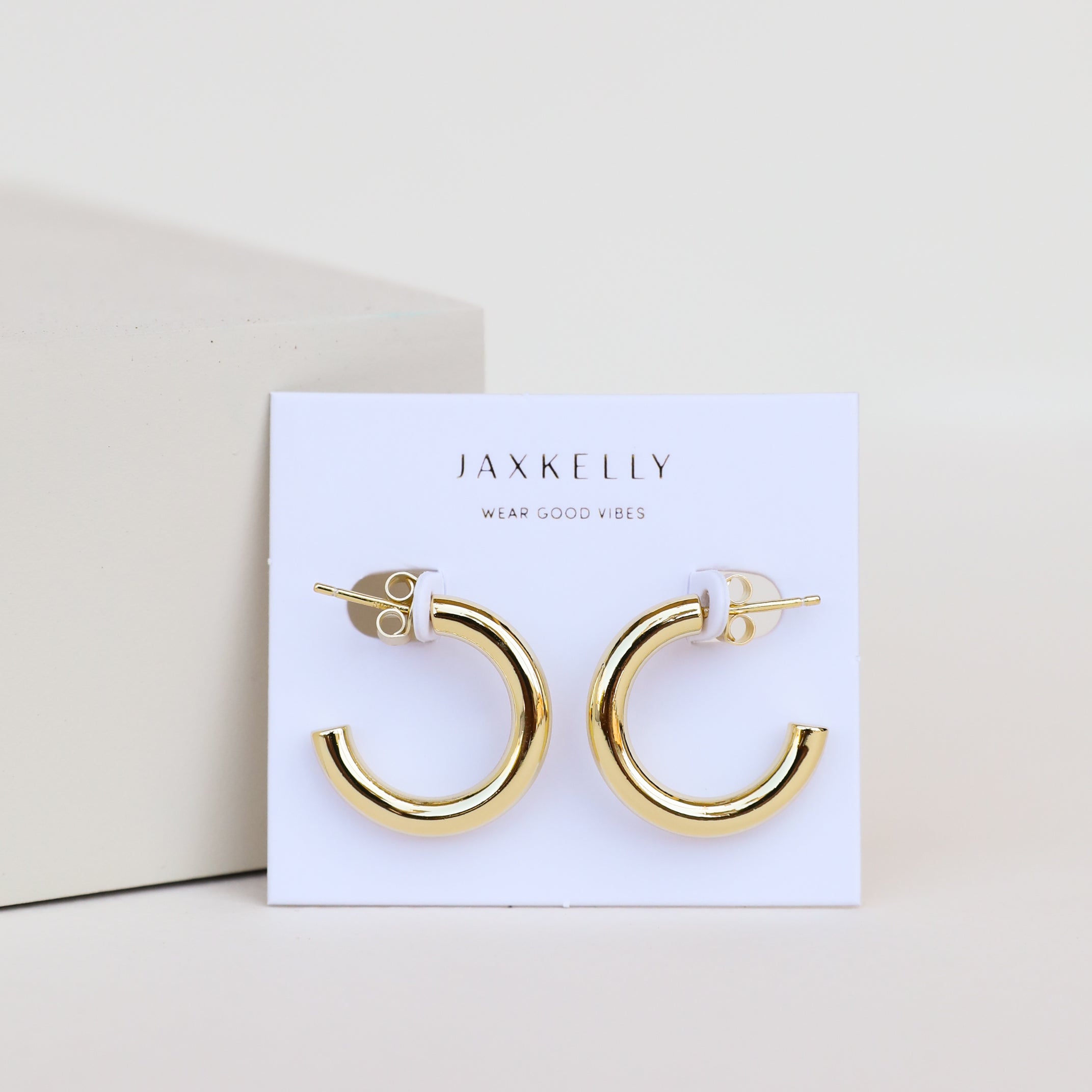 A pair of Gold Hoop - Smooth shiny gold plated earrings displayed on a white card labeled JaxKelly Wear Good Vibes, set against a simple, light background.