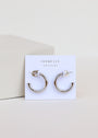 A pair of Silver Hoop - Smooth sterling silver earrings with rhodium plating is displayed on a white JaxKelly card that reads "Wear Good Vibes," set against a minimal pale background.