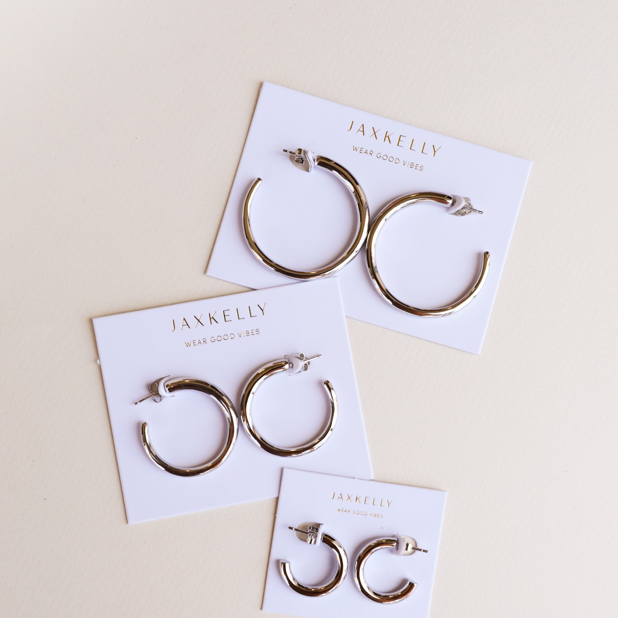 Three pairs of Silver Hoop - Smooth sterling silver earrings in varying sizes are displayed on white JaxKelly Wear Good Vibes cards, arranged on a light beige surface.