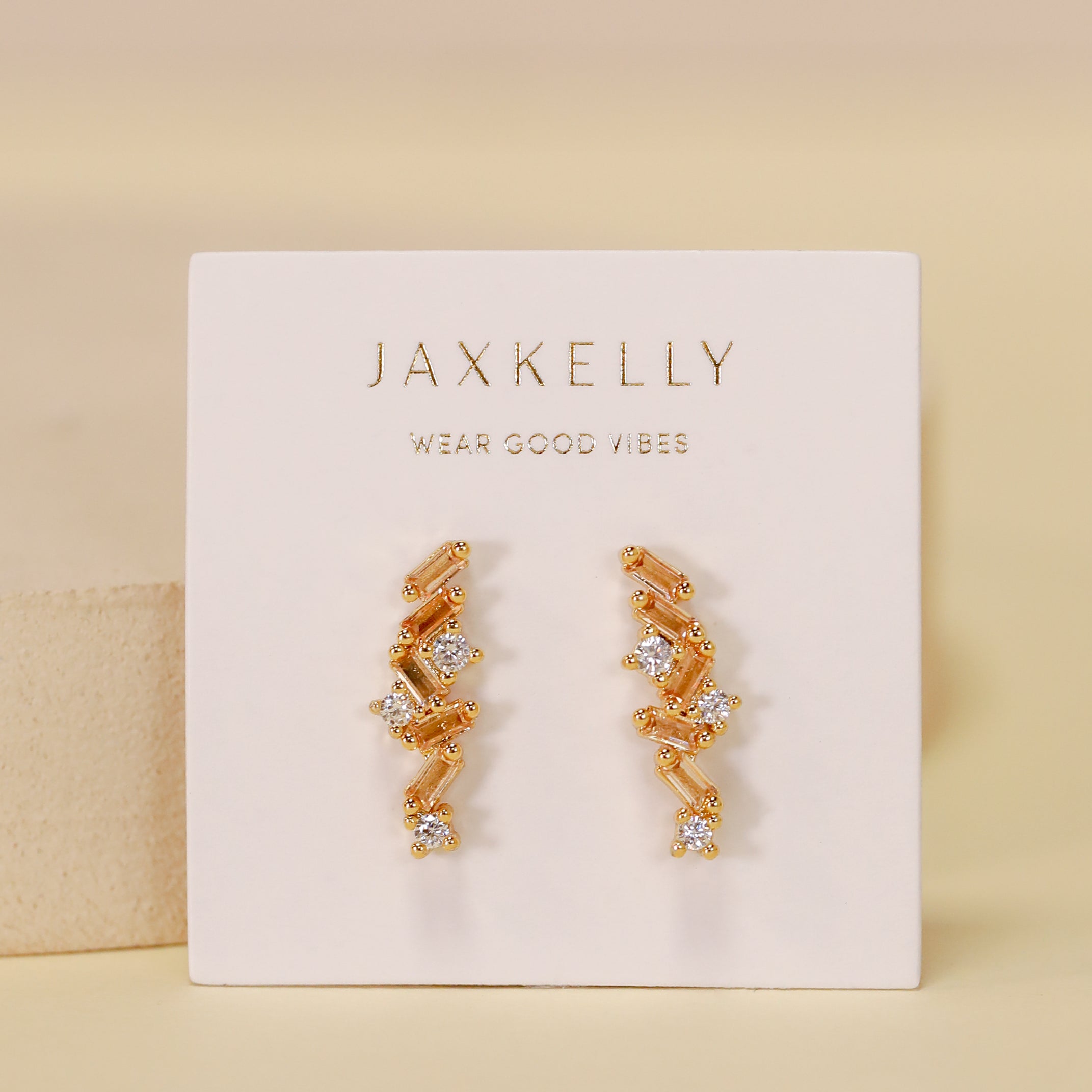 Gold plated Cascading Baguette Drop Earrings with small clear CZ stones are shown on a white JaxKelly Wear Good Vibes card against a soft beige background.