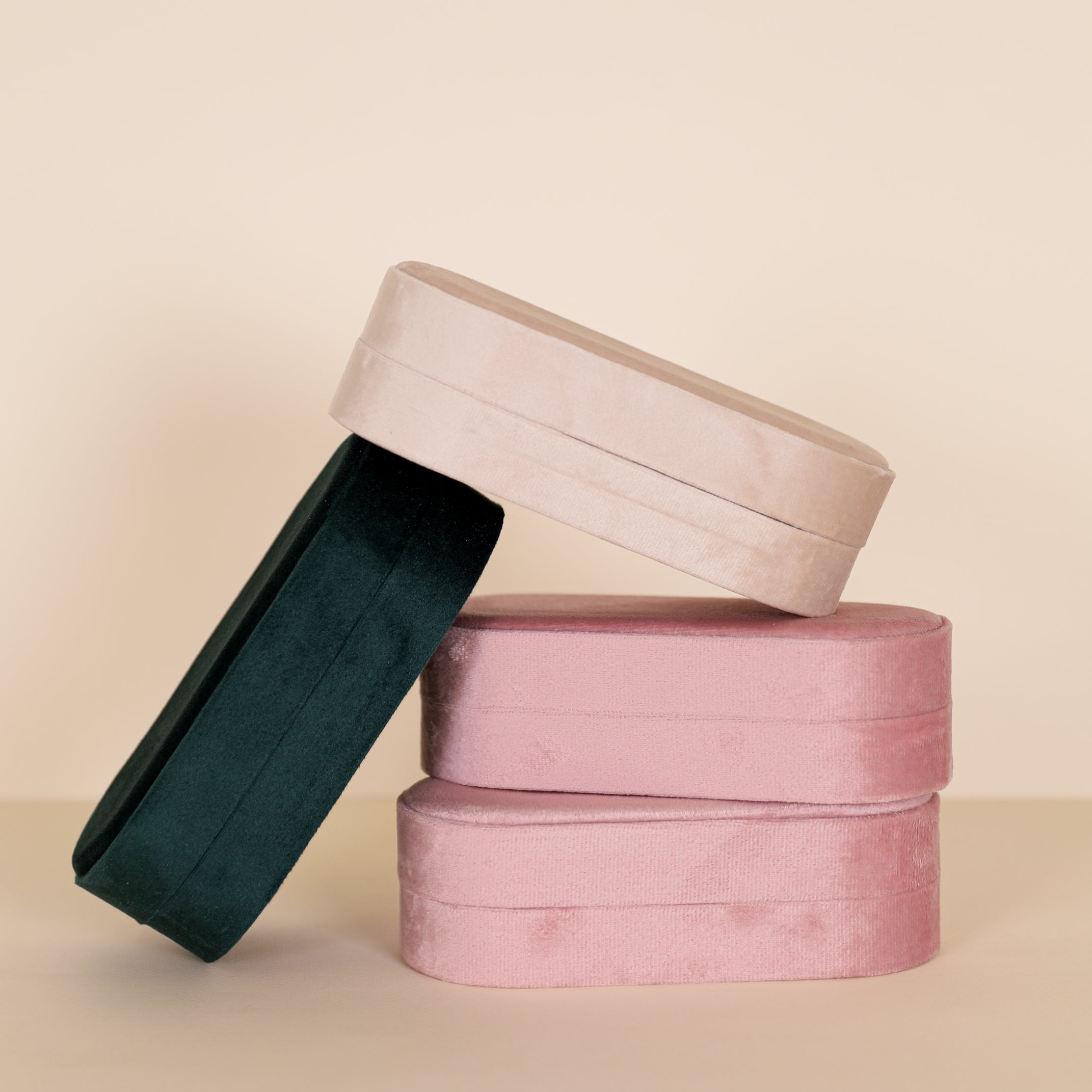 The JaxKelly Large Oval Velvet Jewelry Boxes in light pink are stacked against a beige background, serving as elegant travel organizers or stylish jewelry cases.