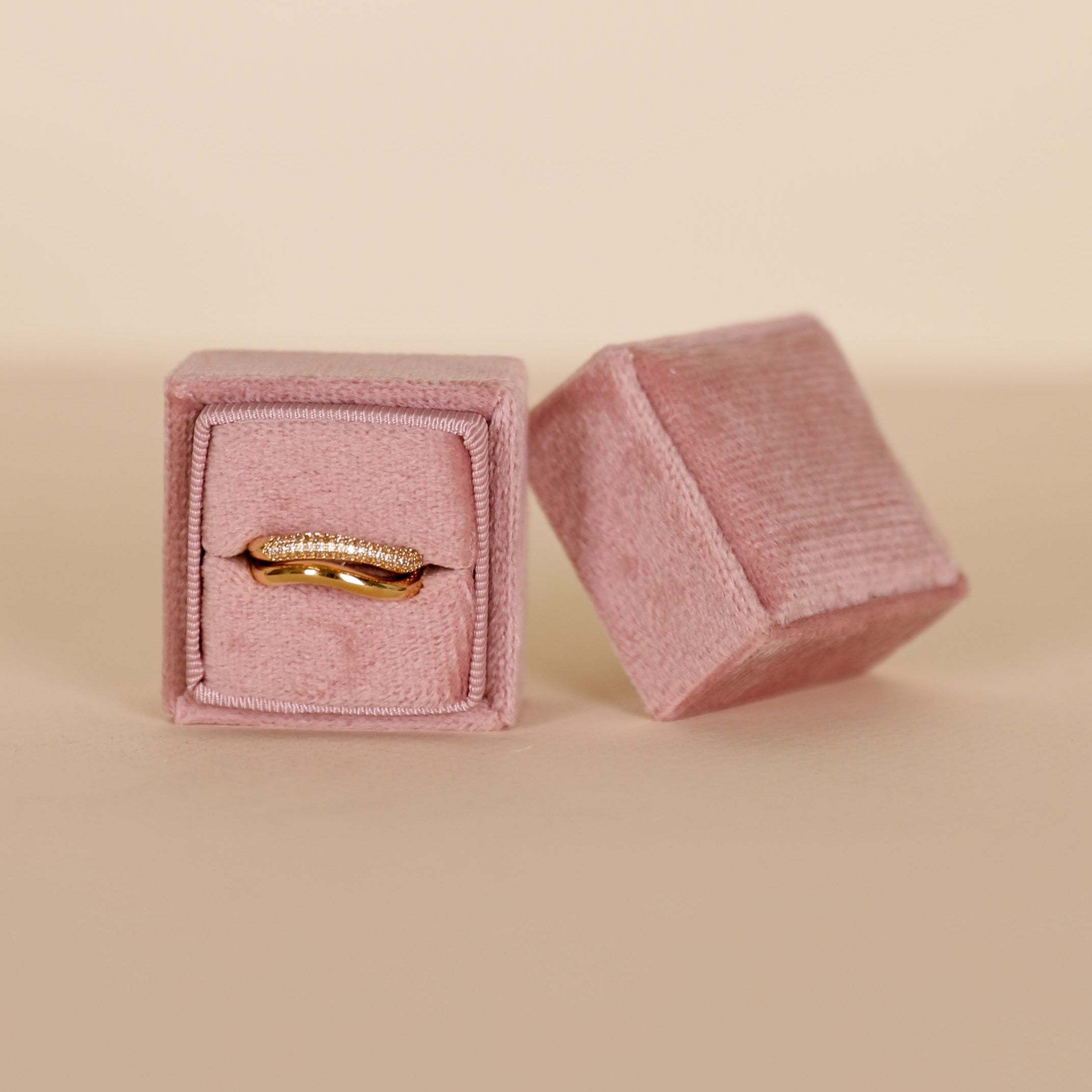 A gold ring with small diamonds is displayed in the JaxKelly Square Velvet Jewelry Box - Light Pink, with its matching lid placed beside it against a neutral background.