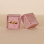 A gold ring with small diamonds is displayed in the JaxKelly Square Velvet Jewelry Box - Light Pink, with its matching lid placed beside it against a neutral background.