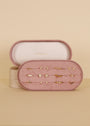 The Large Oval Velvet Jewelry Box in Light Pink by JaxKelly is a travel-friendly organizer that opens to display twelve pairs of small gold earrings—hoops, studs, and more—in neat rows. The inside lid showcases the JaxKelly brand name.