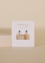 The Open Mini Hoop Earrings - Blue Sapphire feature sapphire CZ stone studs and 18K gold plating, shown on a white JaxKelly card against a neutral beige background.