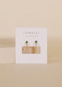 A pair of Open Mini Hoop Earrings - Green Emerald, gold plated with emerald CZ studs, displayed on a white JaxKelly card with gold text against a neutral beige background.