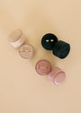 Two JaxKelly Circle Velvet Jewelry Boxes in Light Pink and one in Dark Green hold minimalist earrings and a ring, displayed on a beige surface—perfect for adding to your travel jewelry organizer.