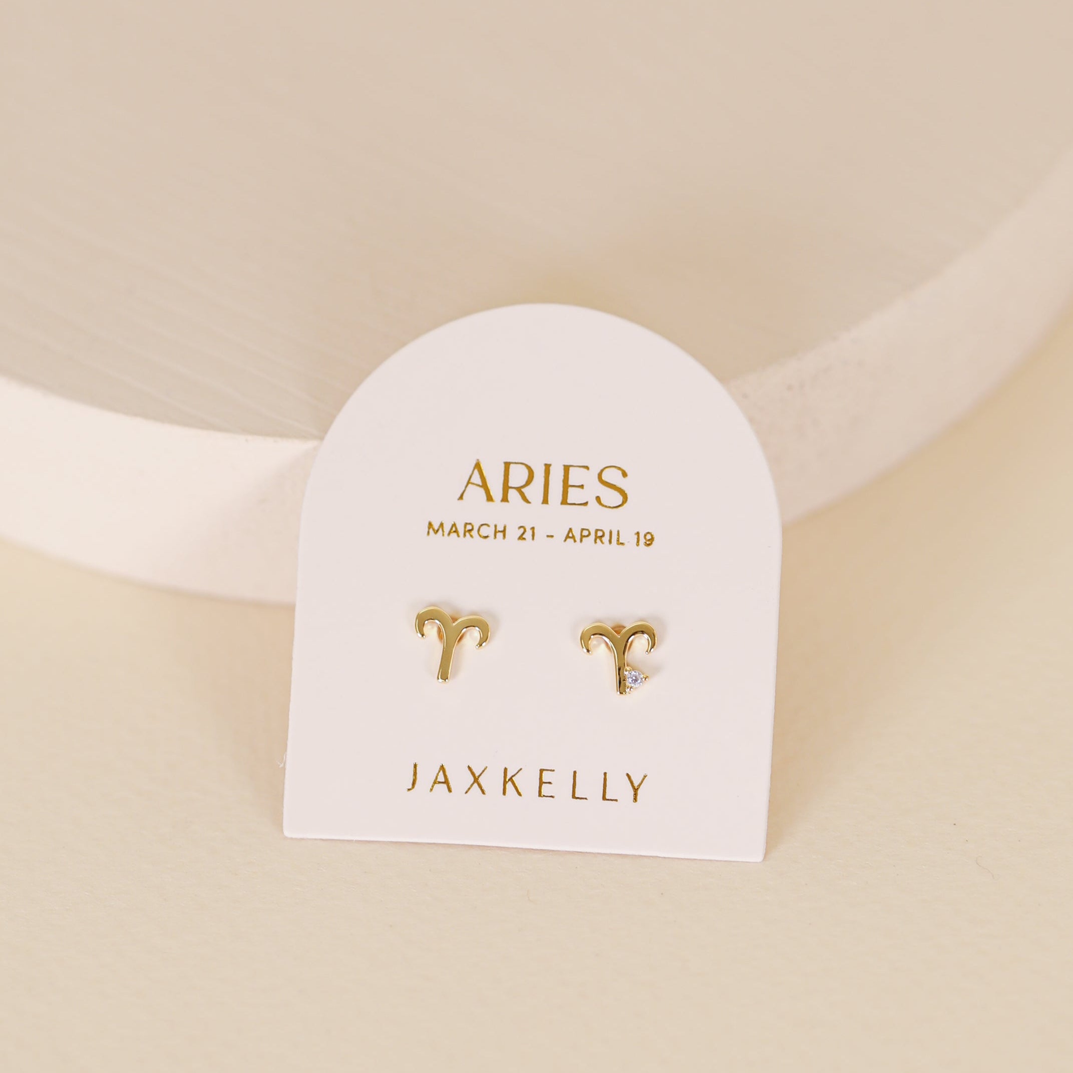 Zodiac Earrings - Aries: Gold plated studs with a small gem and sterling silver posts, shown on a white card labeled “Aries March 21 - April 19” and “JaxKelly,” set against a light neutral background.
