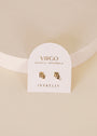 The Zodiac Earrings - Virgo, plated in 18k gold, are displayed on a white card stating “Virgo, August 23 – September 22, JaxKelly” and propped upright on a cream-colored surface.