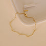 The Gold Ball Bracelet, featuring 18k gold plating, small beads, and an adjustable clasp, is displayed on a light beige textured surface next to an off-white ceramic dish. A tag is attached to the bracelet.