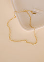 The Small Link Chain Necklace, a delicate gold plated piece with rectangular links, is displayed on a cream-colored surface beside the corner of a square, off-white tray.