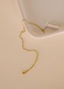 The Simple Twist Chain Bracelet by JaxKelly, featuring a delicate 18K gold plated design with a small tag, rests on a light beige surface beside the corner of a white tray. Its tarnish-free shine ensures lasting beauty for everyday wear.