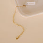 The Small Link Chain Bracelet, featuring an 18k gold plated paper clip design, lobster clasp, and a JAXXELLY white tag, rests on a cream-colored surface beside a ceramic dish.