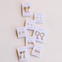 Eight sets of JaxKelly Mystery Earrings, each on a white card with pearls, gold, or rose quartz accents—ideal for earring sales or finding new favorites—all displayed neatly against a light background.