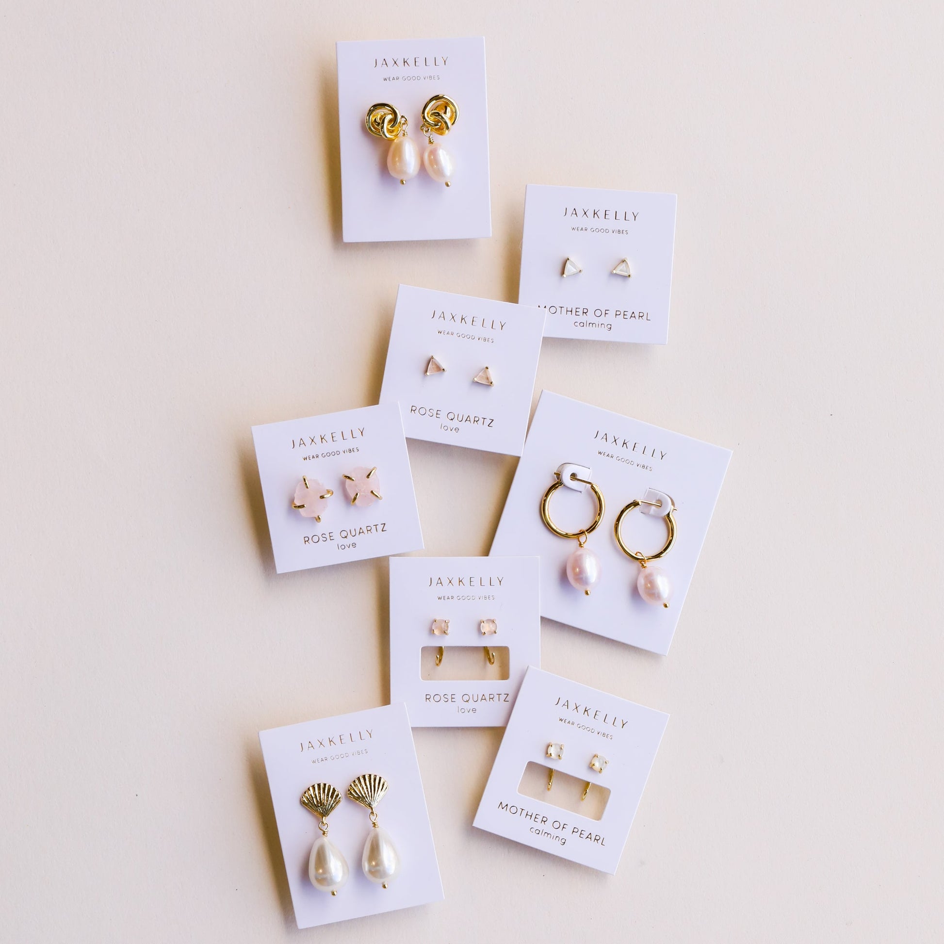 Eight sets of JaxKelly Mystery Earrings, each on a white card with pearls, gold, or rose quartz accents—ideal for earring sales or finding new favorites—all displayed neatly against a light background.