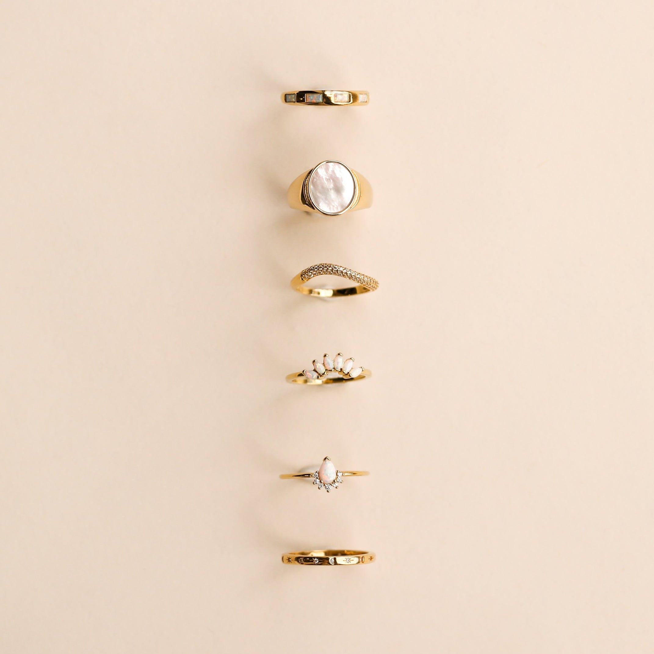 Six JaxKelly Mystery Rings, featuring unique designs like plain bands, pearls, stones, and decorative settings, are arranged vertically on a light beige background—perfect for a ring sale or as a surprise gift.
