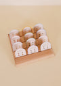 A wooden display stand holds three rows of Birthstone Stud Earring Set - August, each pair mounted on individual white cards with gold text and small designs, arranged neatly against a beige background.