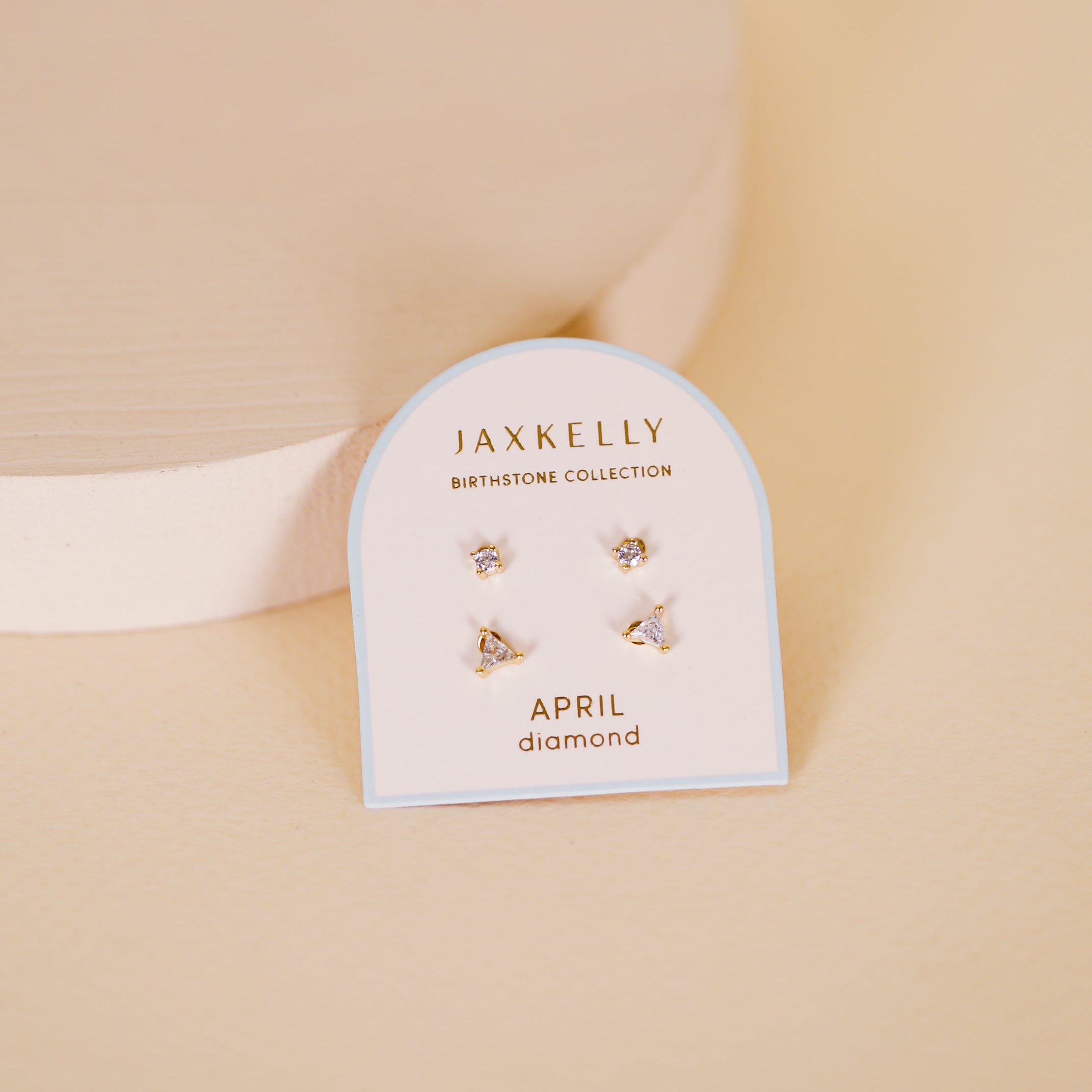 The Birthstone Stud Earring Set - April features three pairs of delicate sterling silver diamond stud earrings, displayed on a JaxKelly Birthstone Collection card labeled April against a soft beige background.