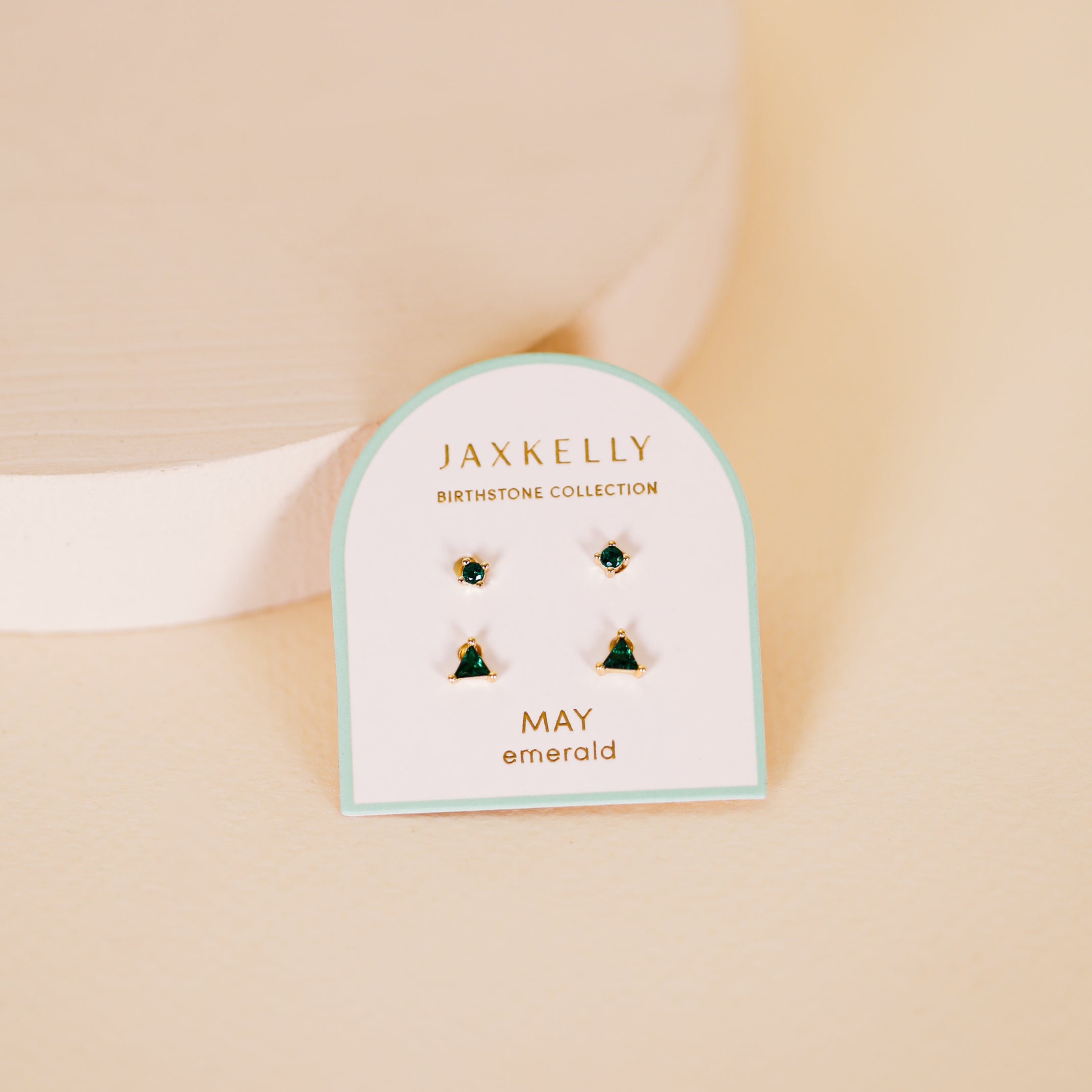 The Birthstone Stud Earring Set - May features four emerald stud earrings on a white card labeled “JaxKelly Birthstone Collection May,” beautifully showcased against a soft beige background.