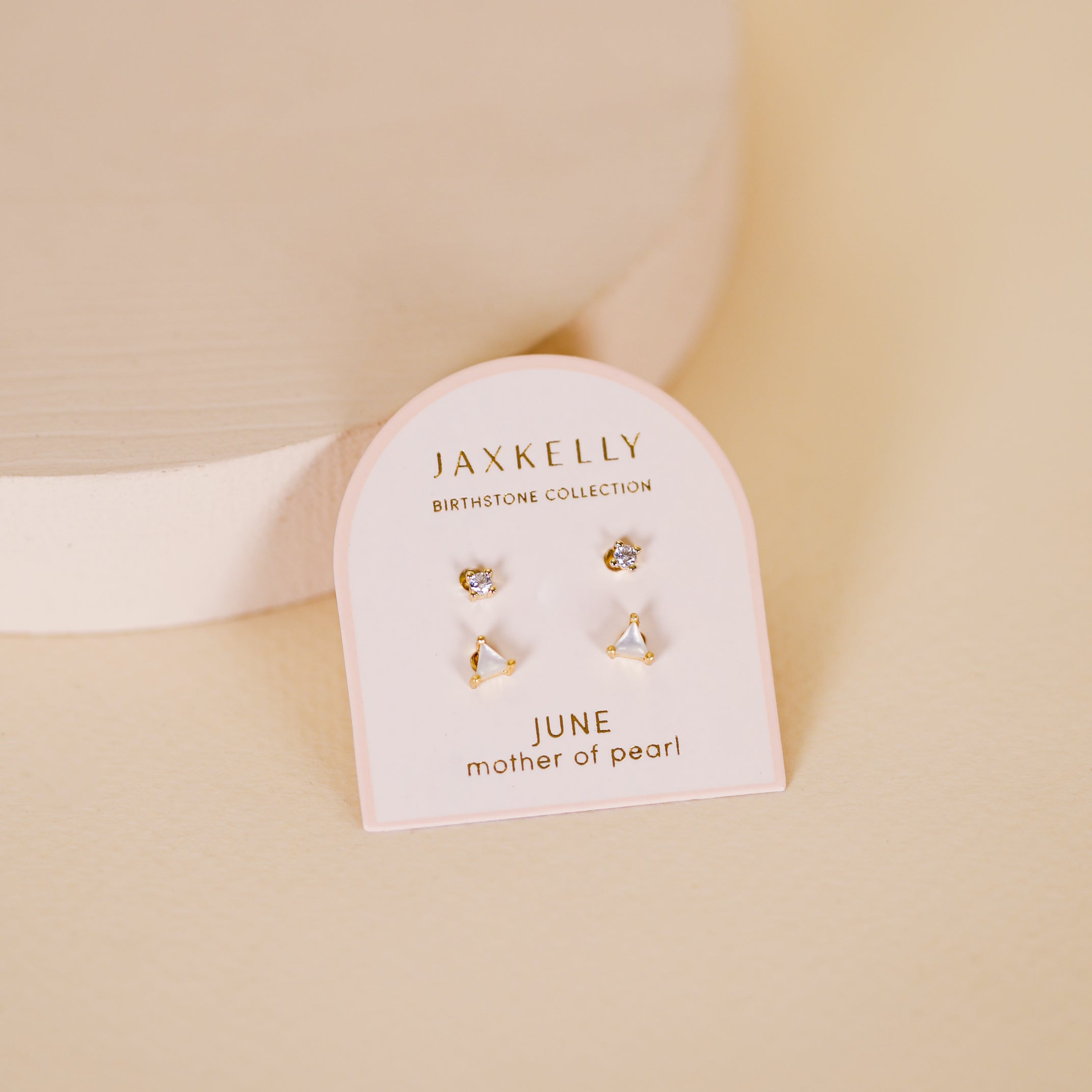A pair of gold plated Birthstone Stud Earring Set - June, featuring pearls on a white JaxKelly Birthstone Collection card labeled "June mother of pearl," displayed on a soft beige surface.