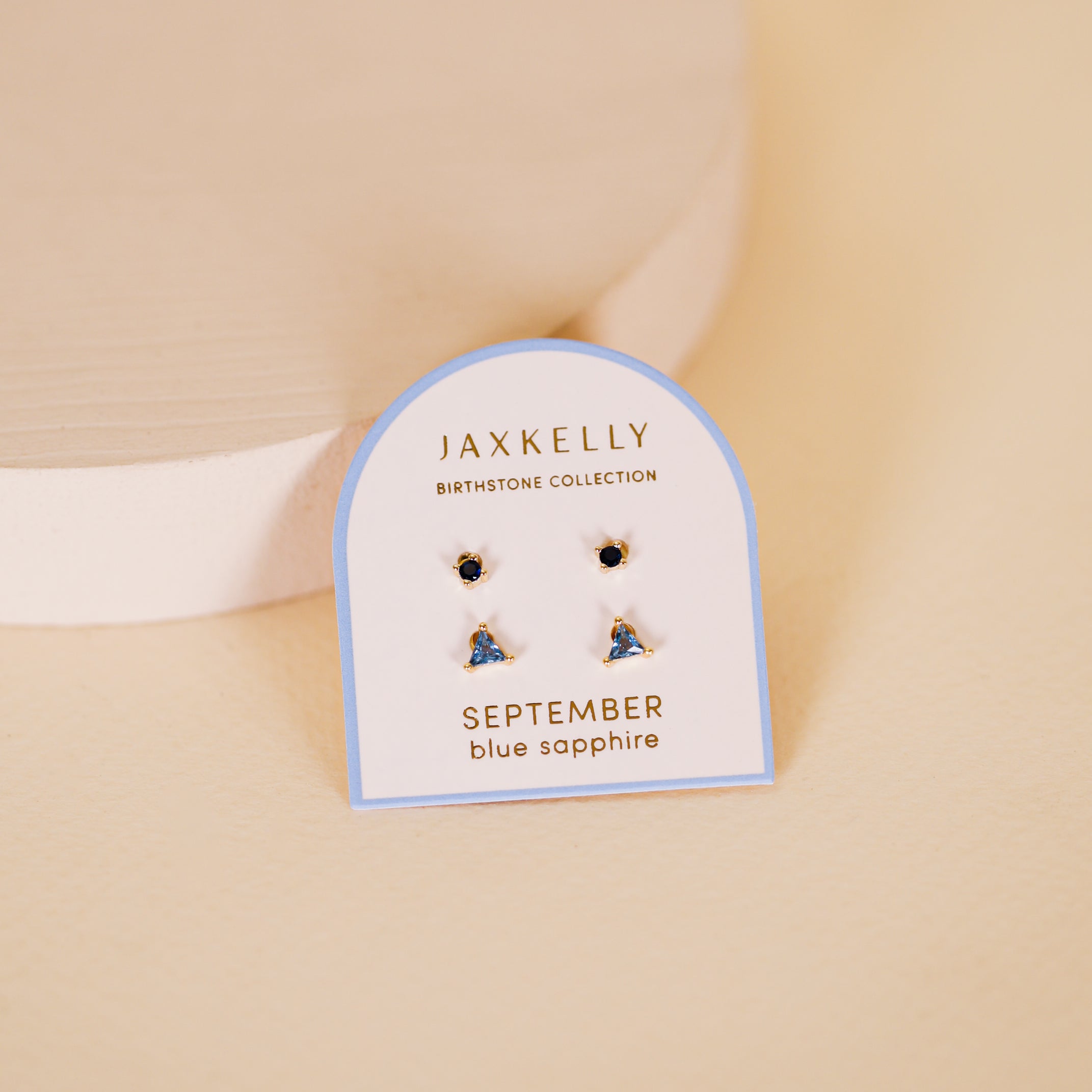 A card labeled Birthstone Stud Earring Set - September displays blue sapphire earrings set in sterling silver, elegantly showcased as September birthstone studs on a light beige surface.